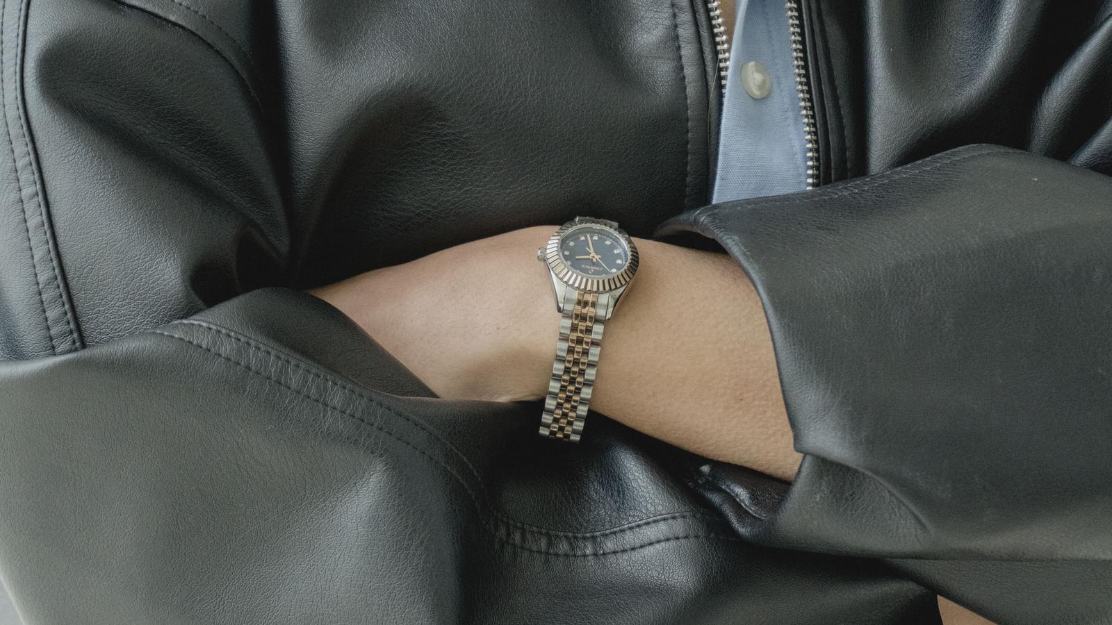 Montre à bracelet acier portée sous une manche de veste en cuir