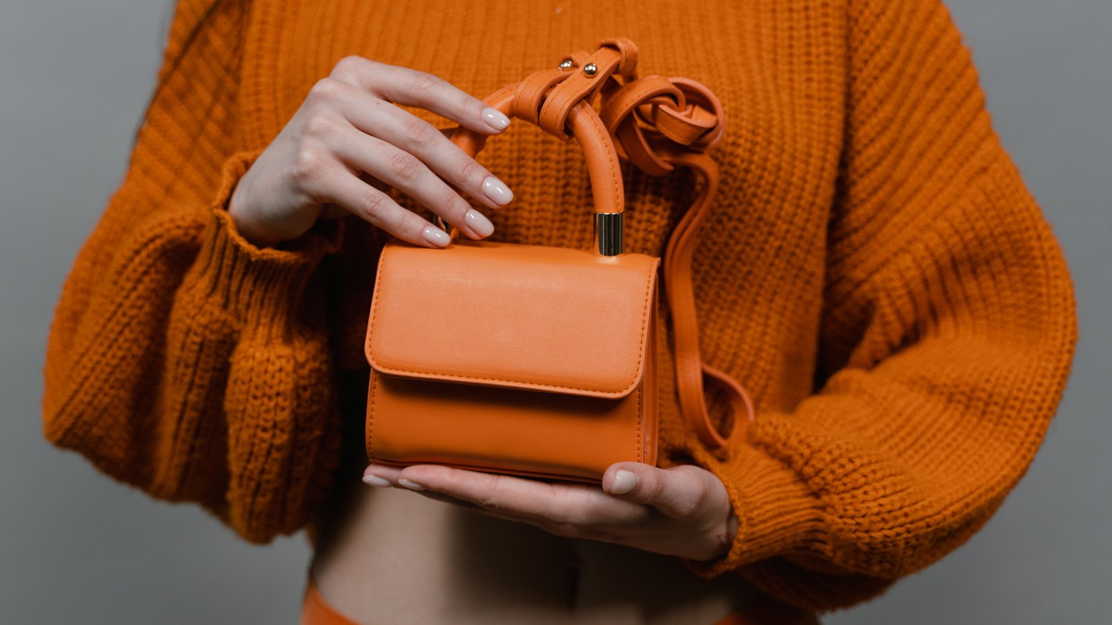 Mini sac orange tenu à deux mains devant un pull en maille