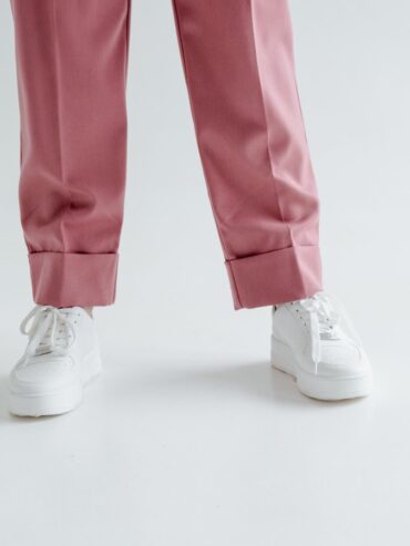 Baskets blanches portées avec un pantalon rose sur fond clair