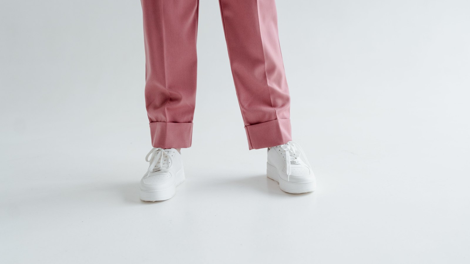 Baskets blanches portées avec un pantalon rose sur fond clair