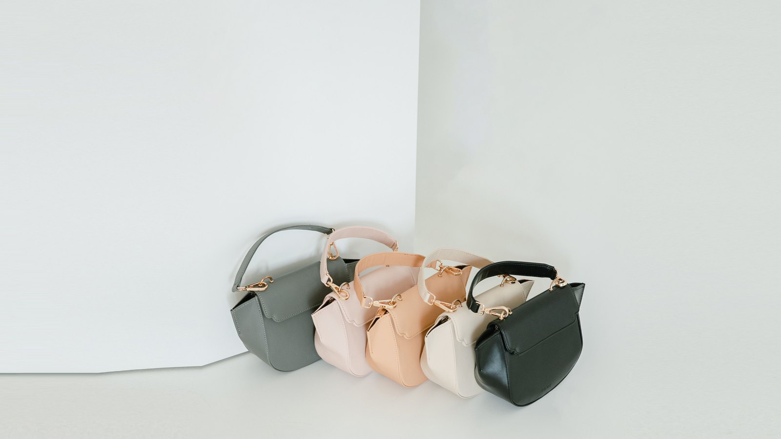 Trois mini sacs alignés, gris, beige et noir, sur fond clair