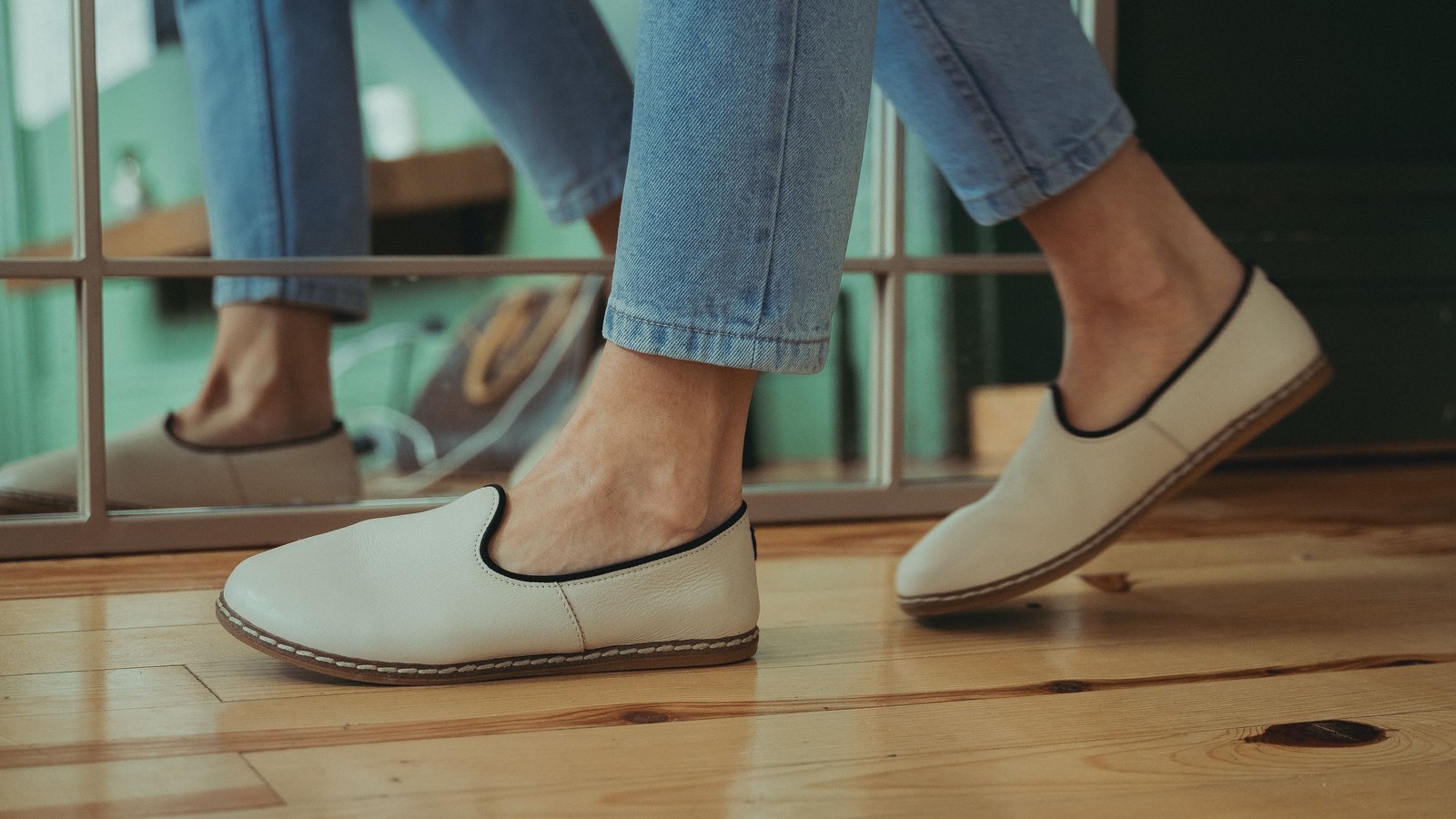 Mocassins crème portés avec un jean clair sur un parquet