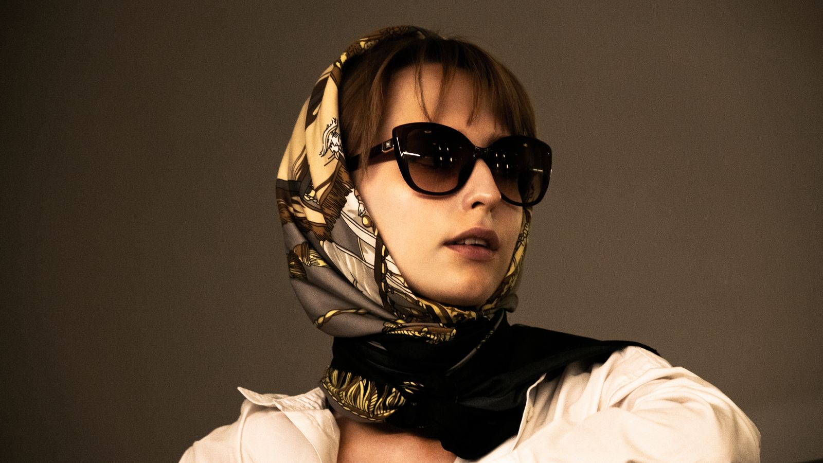 Foulard de soie doré noué sous le menton, porté avec des lunettes noires